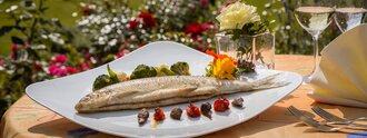 Gebratener Fisch mit Gemüse und Blütendekor auf elegant gedecktem Gartentisch mit Bodenseeblick – feine Küche im Freien beim Hotel Schwedi.