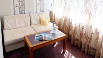 Wohnbereich der Theresia Suite im Hotel Schwedi mit heller Couch, Couchtisch, bodentiefen Fenstern und stilvollen Vorhängen